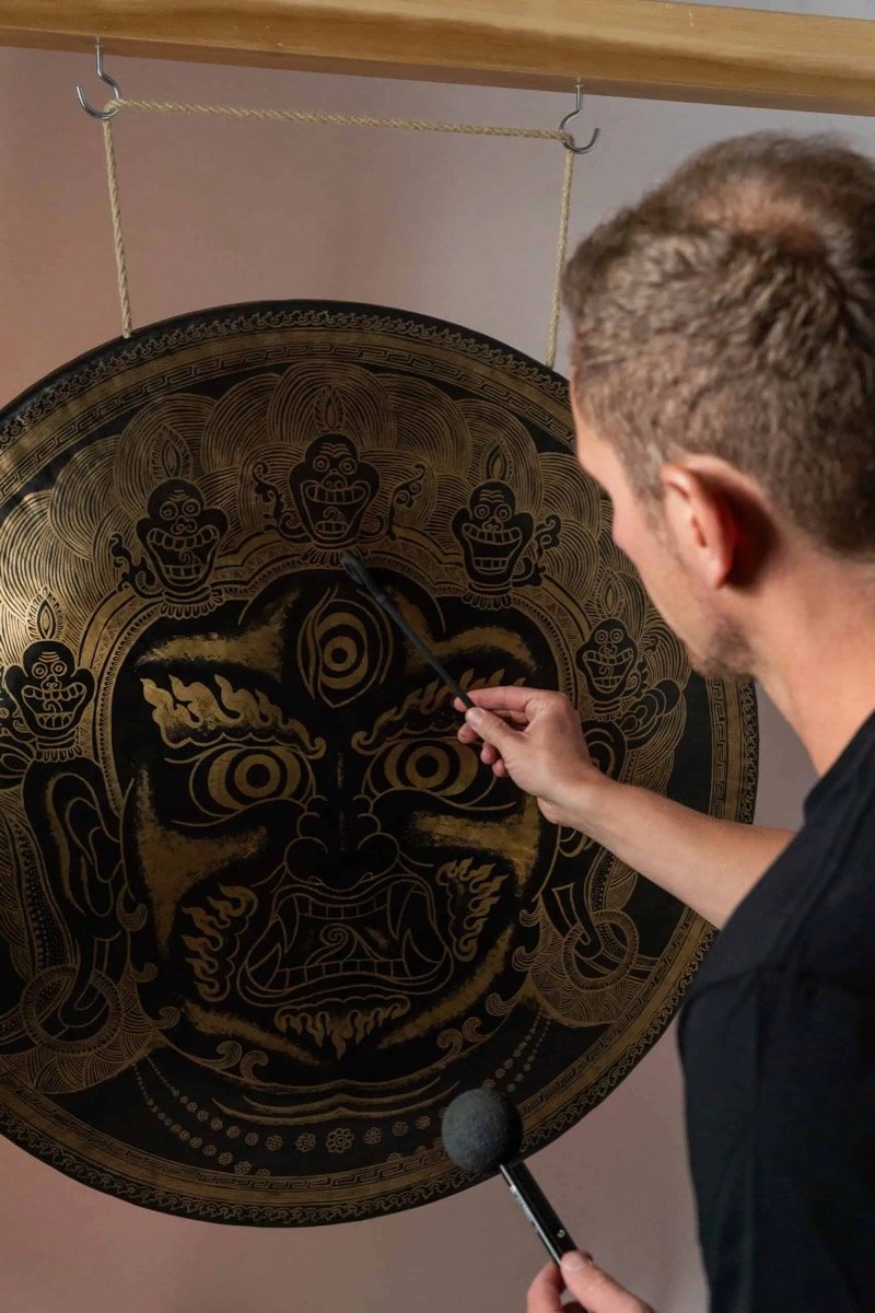 Jens raakt met een mallet een grote gong aan waarop een gouden gravure staat