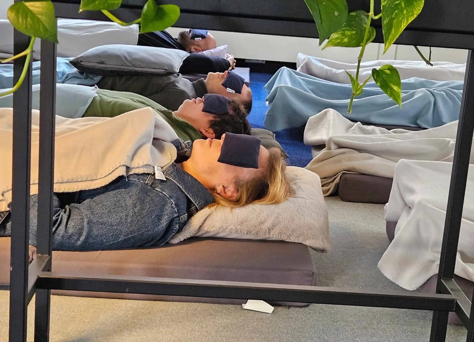 Een team ligt naast elkaar onder dekens met een oogmasker op tijdens een sound bath