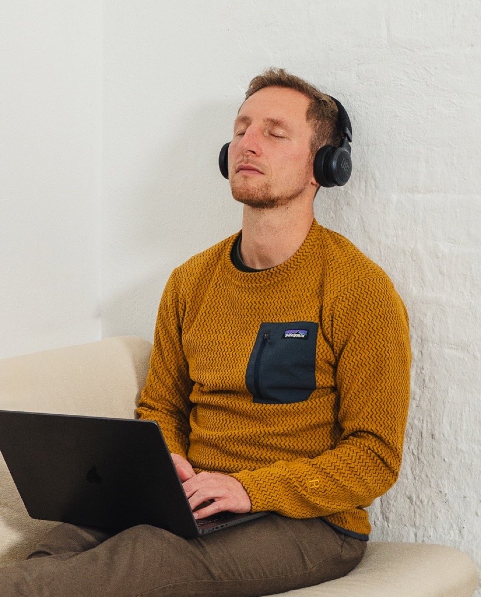 Iemand zit met een laptop op schoot, koptelefoon op en ogen dicht, tijdens een korte pauze